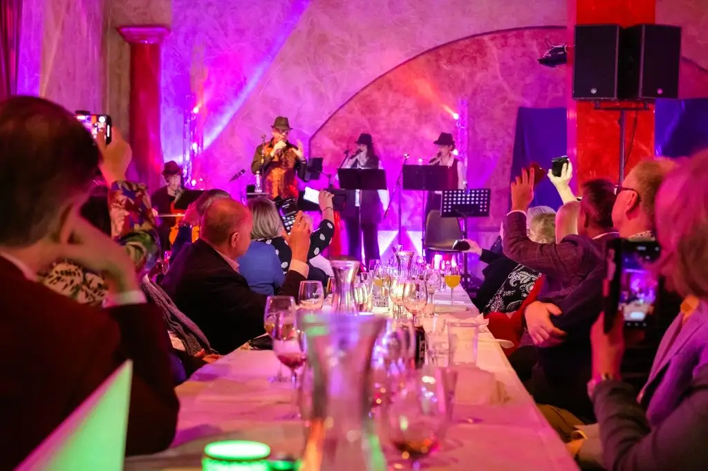 Elämän maku -konsertin yleisö seuraa innokkaasti esiintyjiä lavalla, valaistuna värikkäin lavavaloilla. Monet yleisössä kuvaavat esitystä puhelimillaan pitkien juhlapöytien äärestä.